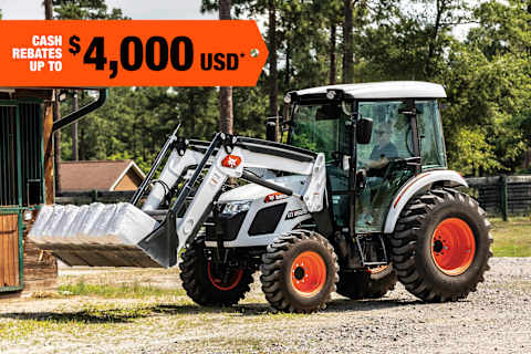 A Utility Tractor Operator Moves Bags of Material Using the Machine’s Bucket; A Cash Rebate Banner Is in the Top-Left Corner