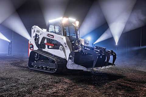 Bobcat T650 compact track loader with lift arms raised under bright work lights