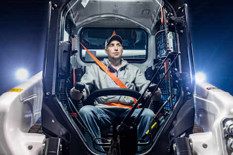 An Operator Uses Joystick Controls Inside a Bobcat T86-2 Compact Track Loader Cab With Interior Lighting and Safety Restraint Engaged
