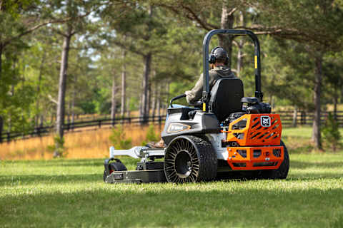 3/4 back beauty shot of Bobcat ZT7000 zero-turn riding mower in action on large acreage property with wooded landscape in the background