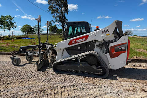 Zijaanzicht van een Bobcat T86 compacte rupslader met een lasergrader-aanbouwdeel die een vlakke ondergrond voorbereidt
