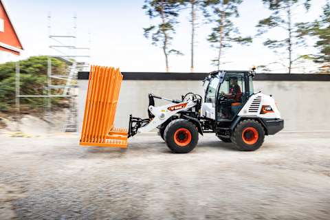 Photo extérieure en action avec le côté de la chargeuse articulée sur pneus Bobcat L85 et un opérateur qui déplacent des barils.