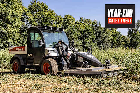 The UW56 Toolcat with Brushcat rotary cutter cutting down tall grasses and brush in field with trees in the background