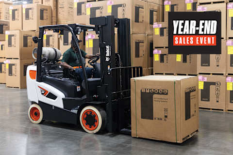 Operador de montacargas Bobcat GC35S-9 moviendo una caja paletizada a través de un almacén con cajas apiladas y gráficos de un evento de ventas de fin de año.