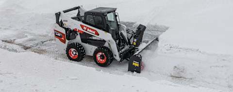 Front right quarter view of an operator removing snow using a snowblower attached to a Bobcat S86 Skid-Steer Loader 
