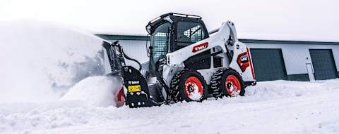Left side view of an operator removing snow using a snowblower attached to a Bobcat S590 Skid-Steer Loader 