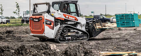 Right side view of an operator hauling wood using an industrial grapple attached to a Bobcat T64 Compact Track Loader 