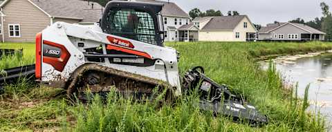 Right side view of an operator using a Brushcat attached to a Bobcat T550 Compact Track Loader 