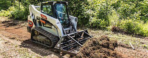 Front right quarter view of an operator using a landplane attached to a Bobcat T595 Compact Track Loader