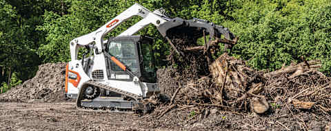 Right side view of an operator clearing brush using an industrial grapple attached to a Bobcat T650 Compact Track Loader 