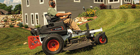 Male homeowner mowing uphill around curved landscape on side of house with Bobcat ZT3000 zero-turn riding mower