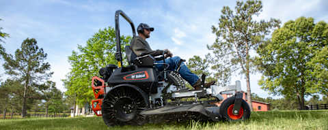 Low angle side profile action mowing shot of Bobcat ZT7000 zero-turn riding mower with male operator mowing large acreage horse ranch property