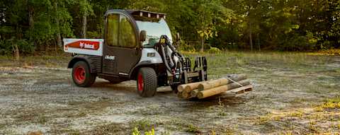 Bobcat UW56 Toolcat utility work machine with pallet fork attachment transporting wood posts on rural property
