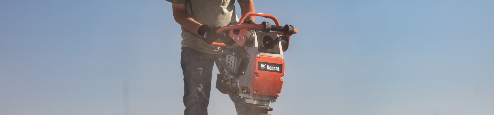 Operator using the Bobcat Rammer to compact dirt in trenches.