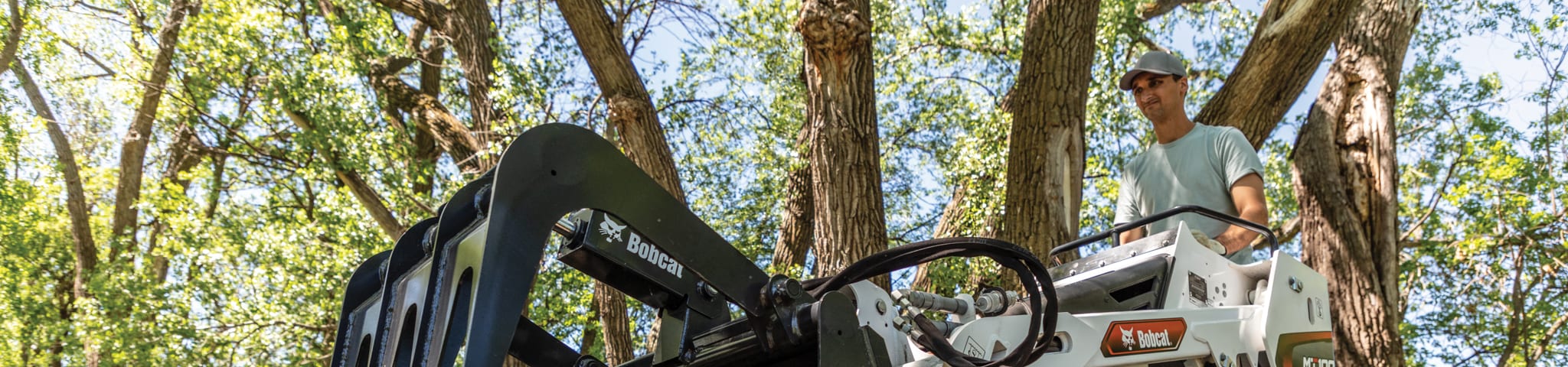 A Bobcat MT100 Mini Track Loader With Industrial Grapple Attachment Working In Wooded Area