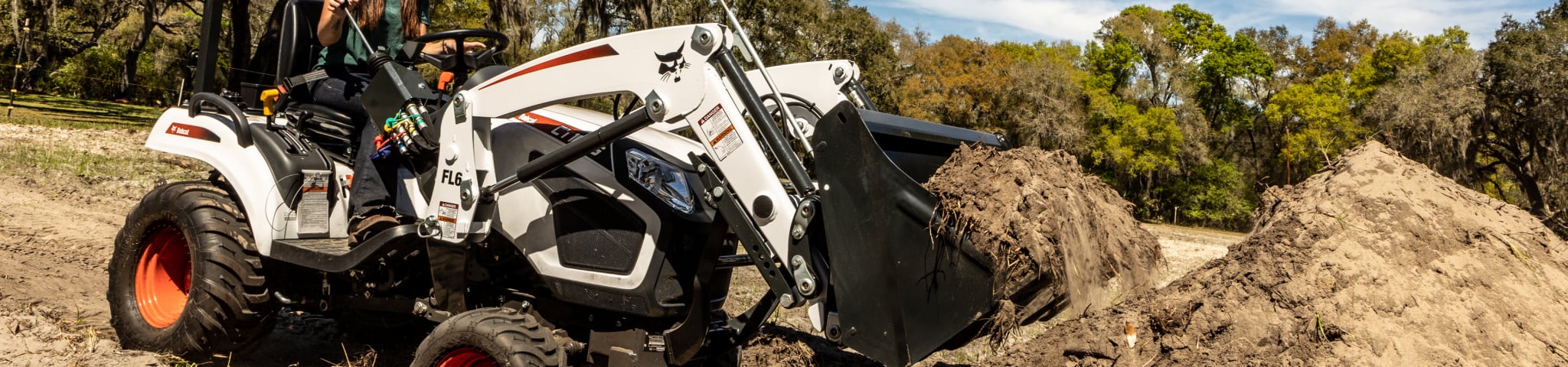 Operator uses a Bobcat sub compact tractor with front-end loader to move dirt 