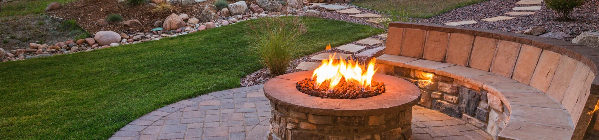 A Beautifully Landscaped Backyard Firepit Surrounded by a Stonework Bench