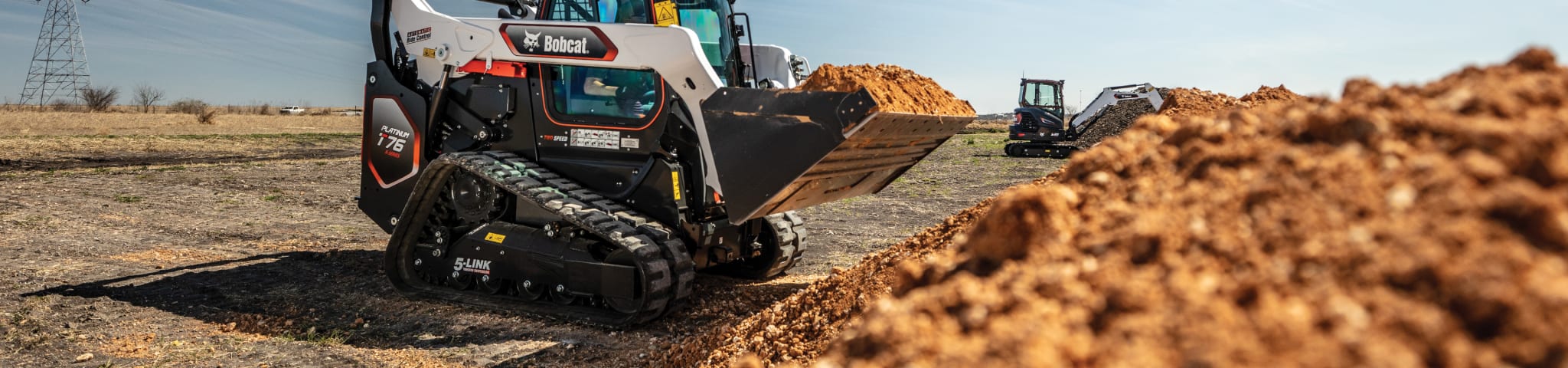 A Bobcat Platinum Package Compact Track Loader and Platinum Package Compact Excavator Loading Dirt in an Outdoor Infrastructure Jobsite