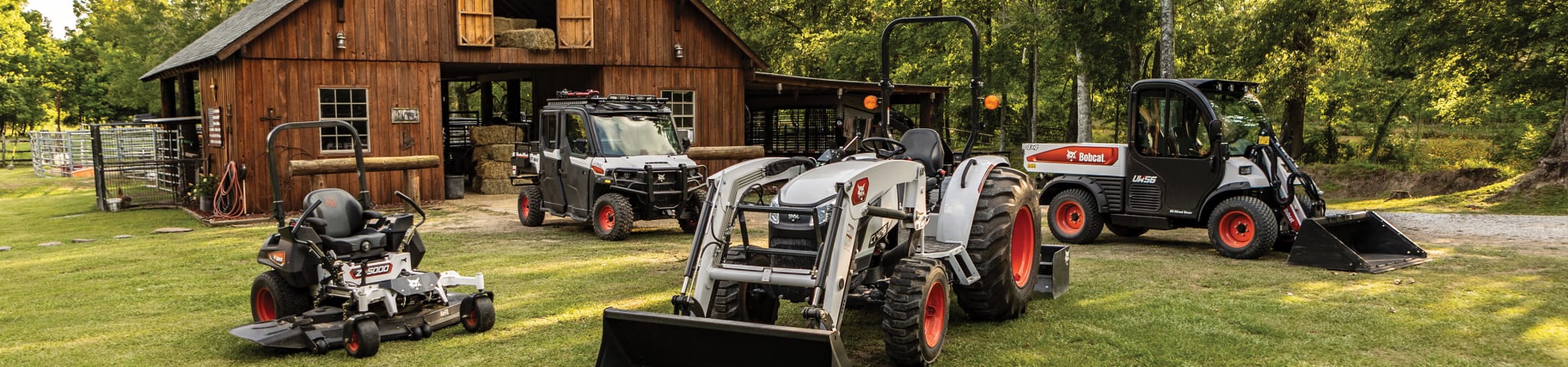 A Lineup of Bobcat Equipment in Front of a Large Barn, Including a Bobcat Zero-Turn Mower, Bobcat Utility Vehicle, Bobcat Compact Tractor and Toolcat Utility Work Machine