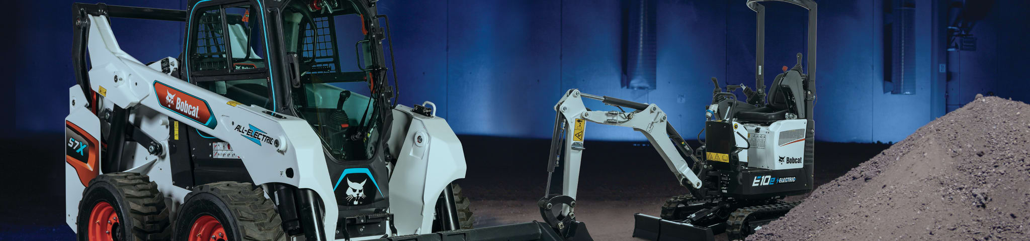 Bobcat S7x Skid-Steer Loader and E10e Battery Electric Compact Excavator Beside Each Other Indoors.