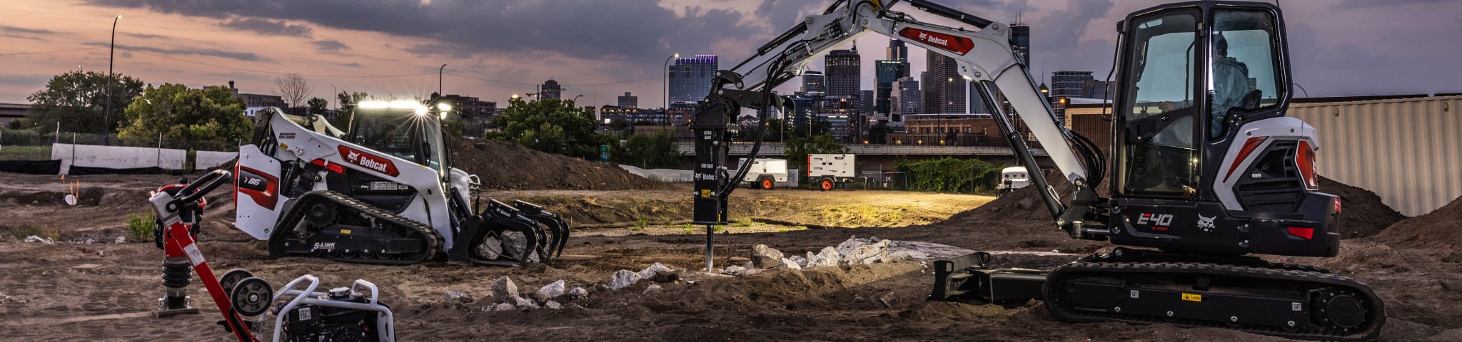 A Lineup of Bobcat Equipment Working at Dusk on an Urban Construction Site
