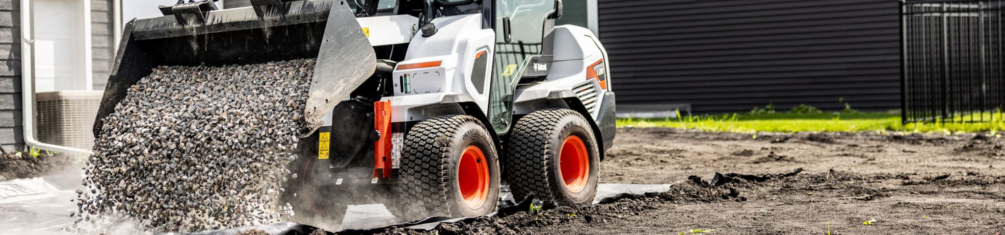 A Bobcat L28 Small Articulated Loader With a Bucket Attachment Dumps Rocks in a Residential Yard