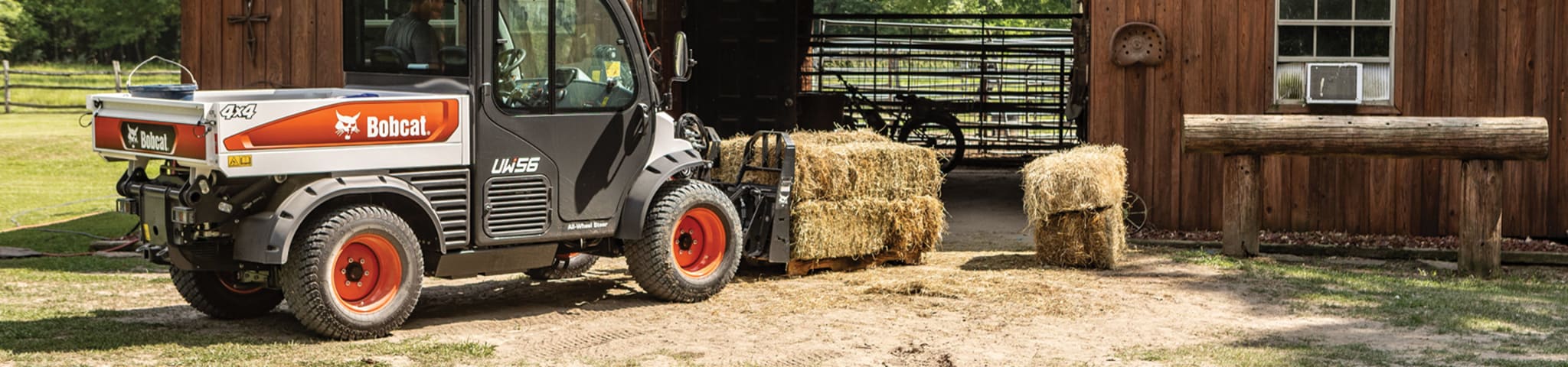 A Toolcat UW56 Utility Work Machine With a Pallet Fork Attachment Moves Hay Bales Around a Barn