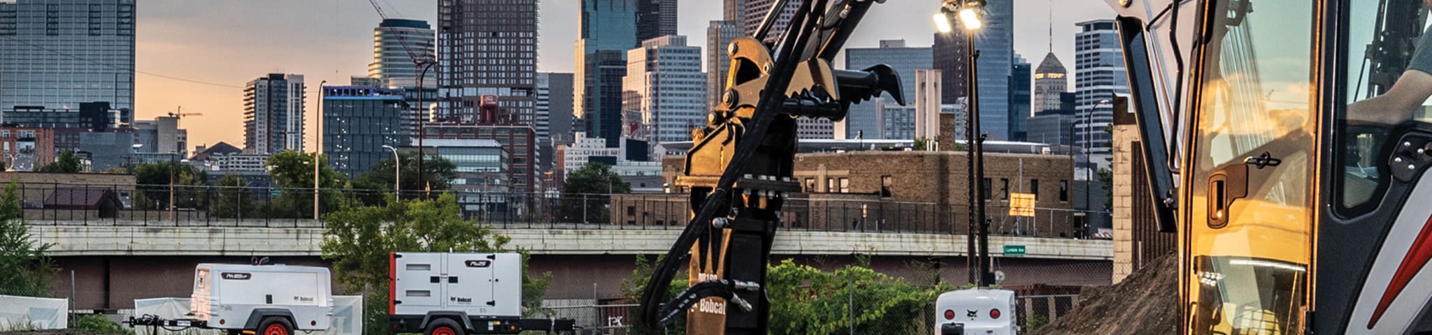 An Urban Jobsite With a Bobcat Portable Generator, Portable Air Compressor and Portable Light Tower. A Bobcat Compact Excavator Works in the Foreground. 