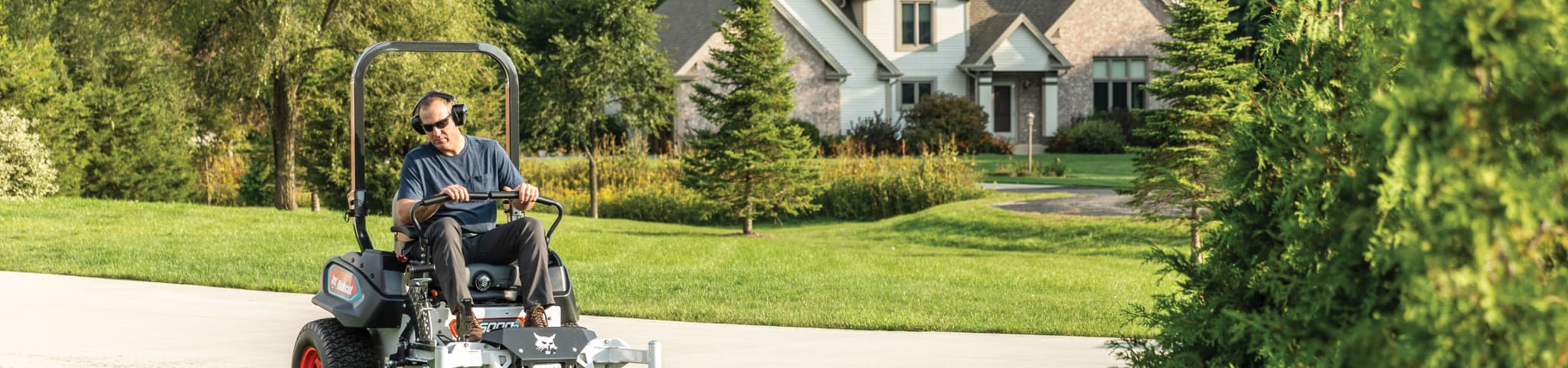 Operator uses a Bobcat ZT6000e to cut grass near a driveway