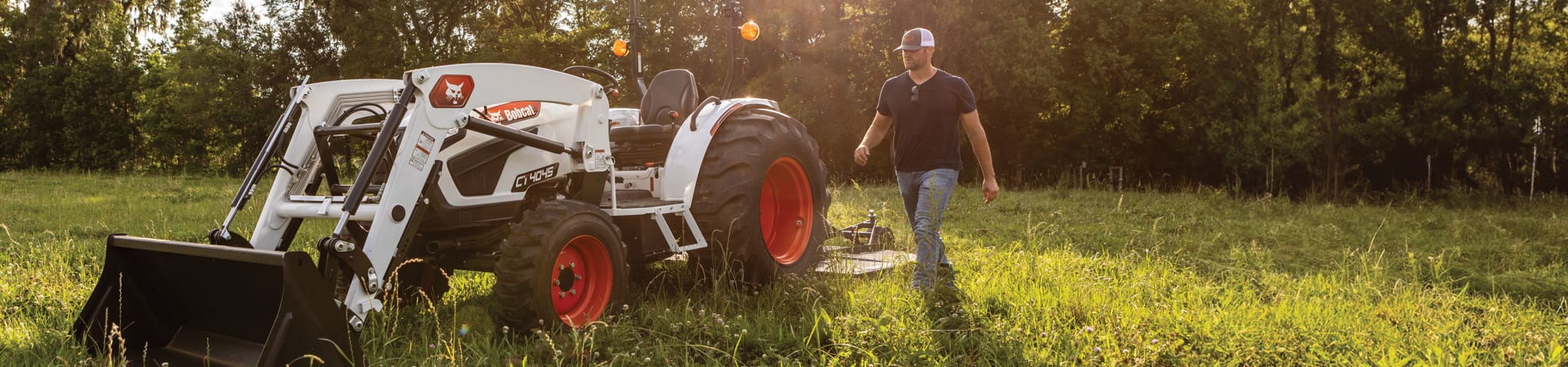 An Operator Walks Near a Bobcat CT4045 Compact Tractor with Front-End Loader and 3-Point Rotary Cutter Implement in Pasture