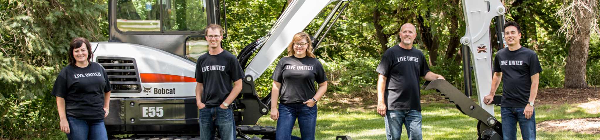 Bobcat United Way Team Posing In Front Of A Mini Excavator