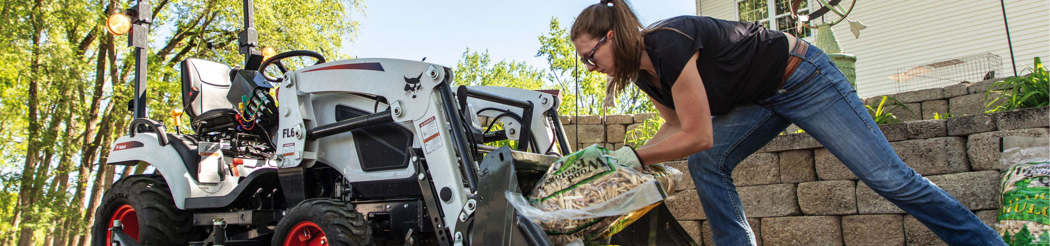 A Woman Loads Bags of Mulch Into the Bucket of a Bobcat CT1025 Sub-Compact Tractor