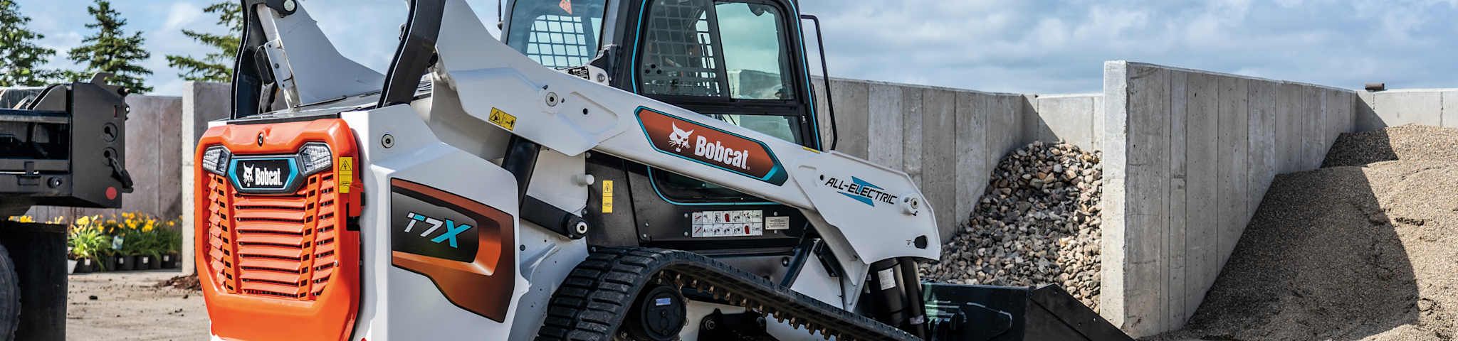  A Bobcat T7X Electric Compact Track Loader with a severe duty bucket attachment with an operator hauling gravel at a commercial construction site.