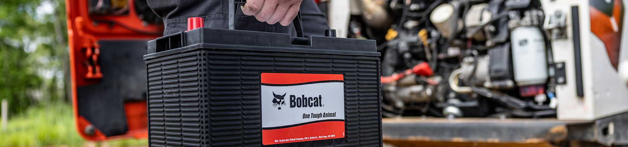 A Person Carries a Bobcat Battery Toward a Bobcat Loader