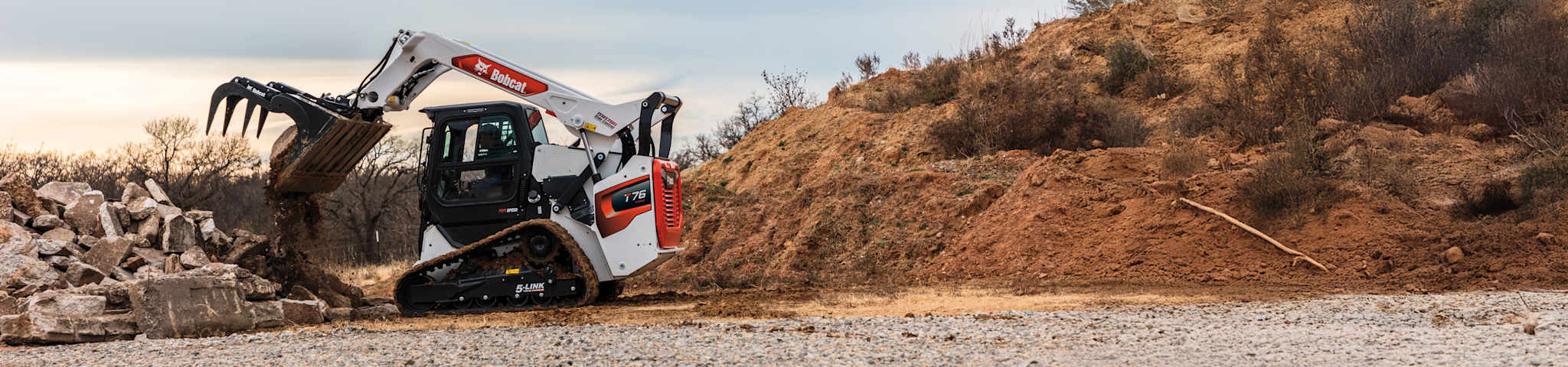 Left side view of an operator clearing debris at a commercial construction site using an industrial grapple attached to a Bobcat T76 Compact Track Loader