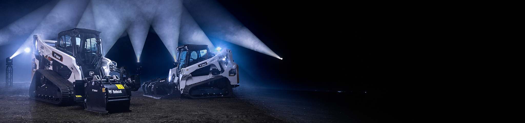 Two Bobcat Compact Track Loaders a T86-2 With a Planer Attachment and a T650 With a Grapple Attachment Positioned on a Dirt Surface Under Dramatic Lighting