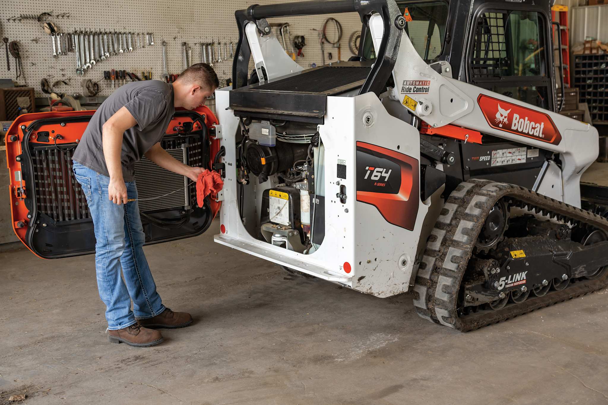 Technician servicing a Bobcat T64 loader in a workshop, highlighting dealer maintenance and support capabilities.