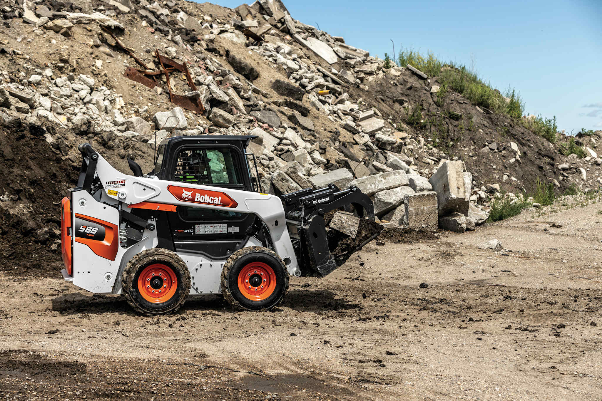 Bobcat S66 skid steer loader transporting debris on a demolition jobsite using a grapple.