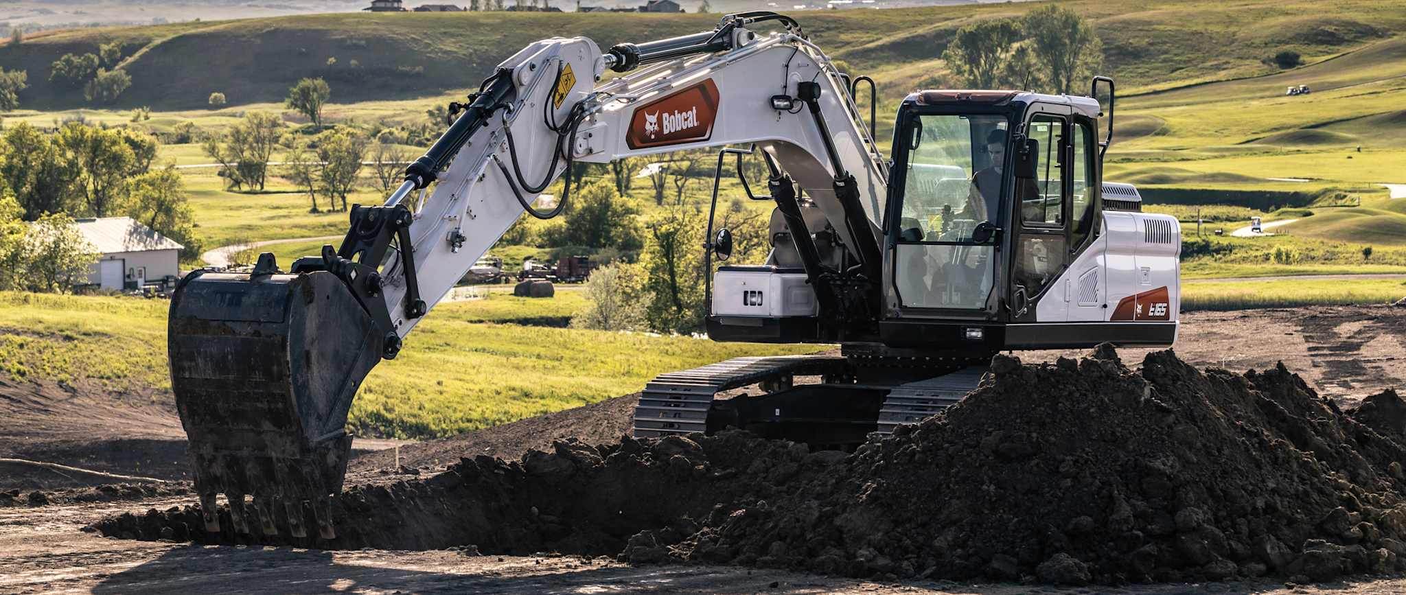 Bobcat e165 Large Excavator Digs Dirt With Grassy Hills in Background