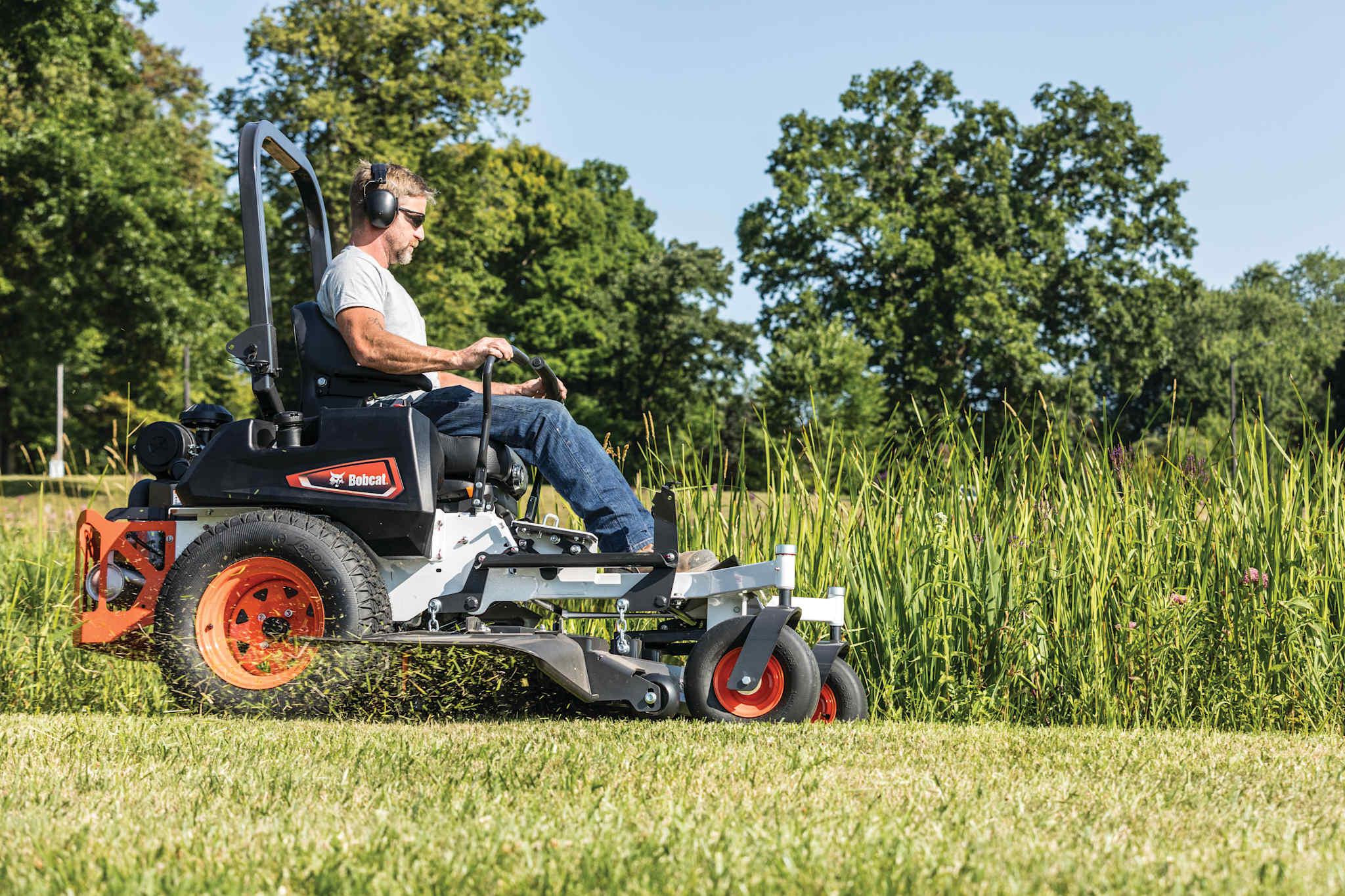 Professional operator on Bobcat ZT5000 zero-turn riding mower cutting grass in park with grass clippings flying out of mower deck
