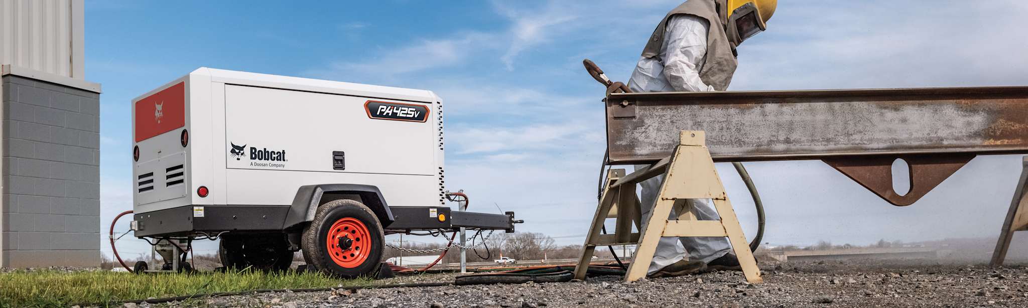 Worker Standing Next to Metal Beam on Sawhorse with Bobcat PA425v Portable Air Compressor in Background