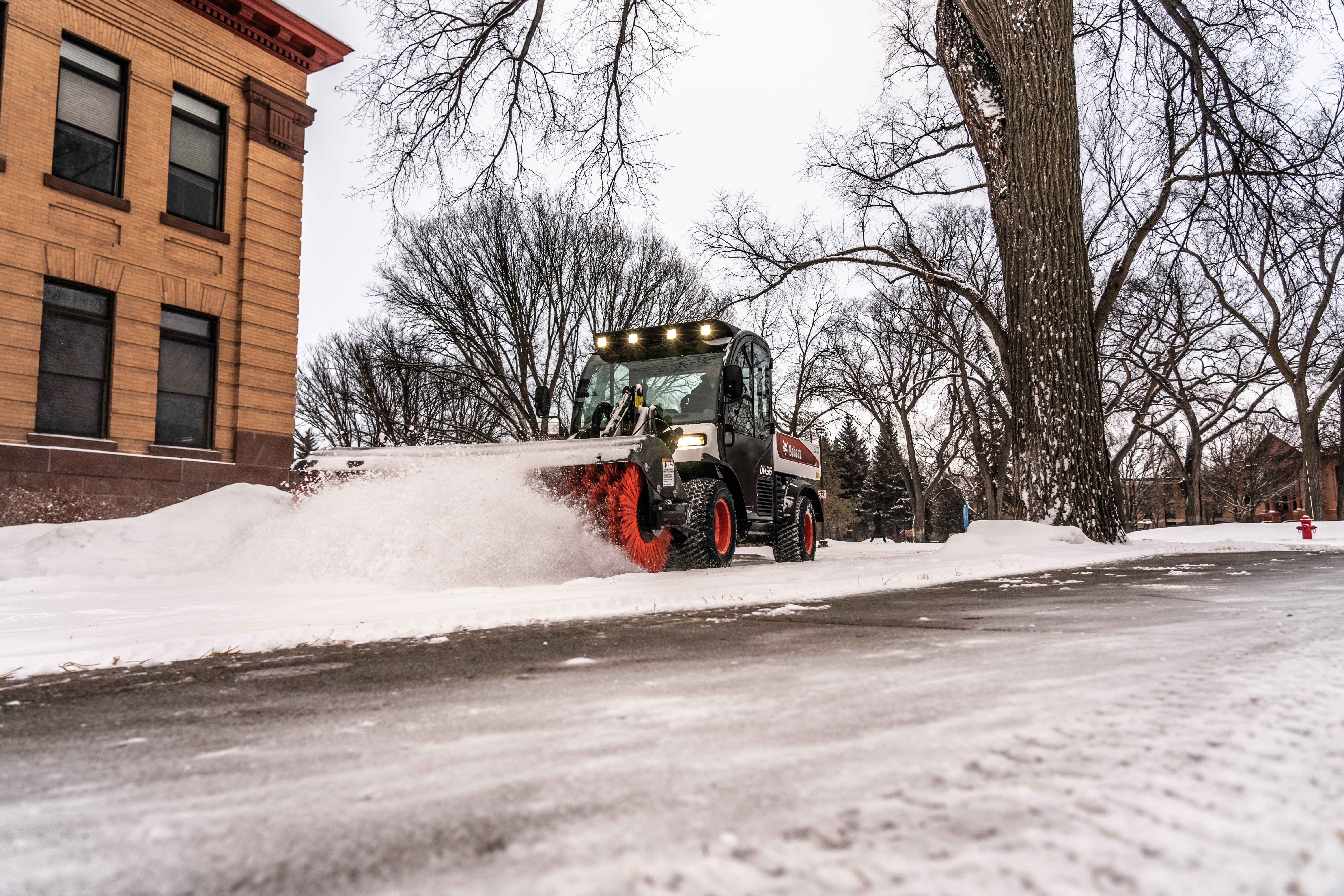An Operator Uses a Toolcat Utility Work Machine and an Angle Broom Attachment to Move Snow From a Sidewalk