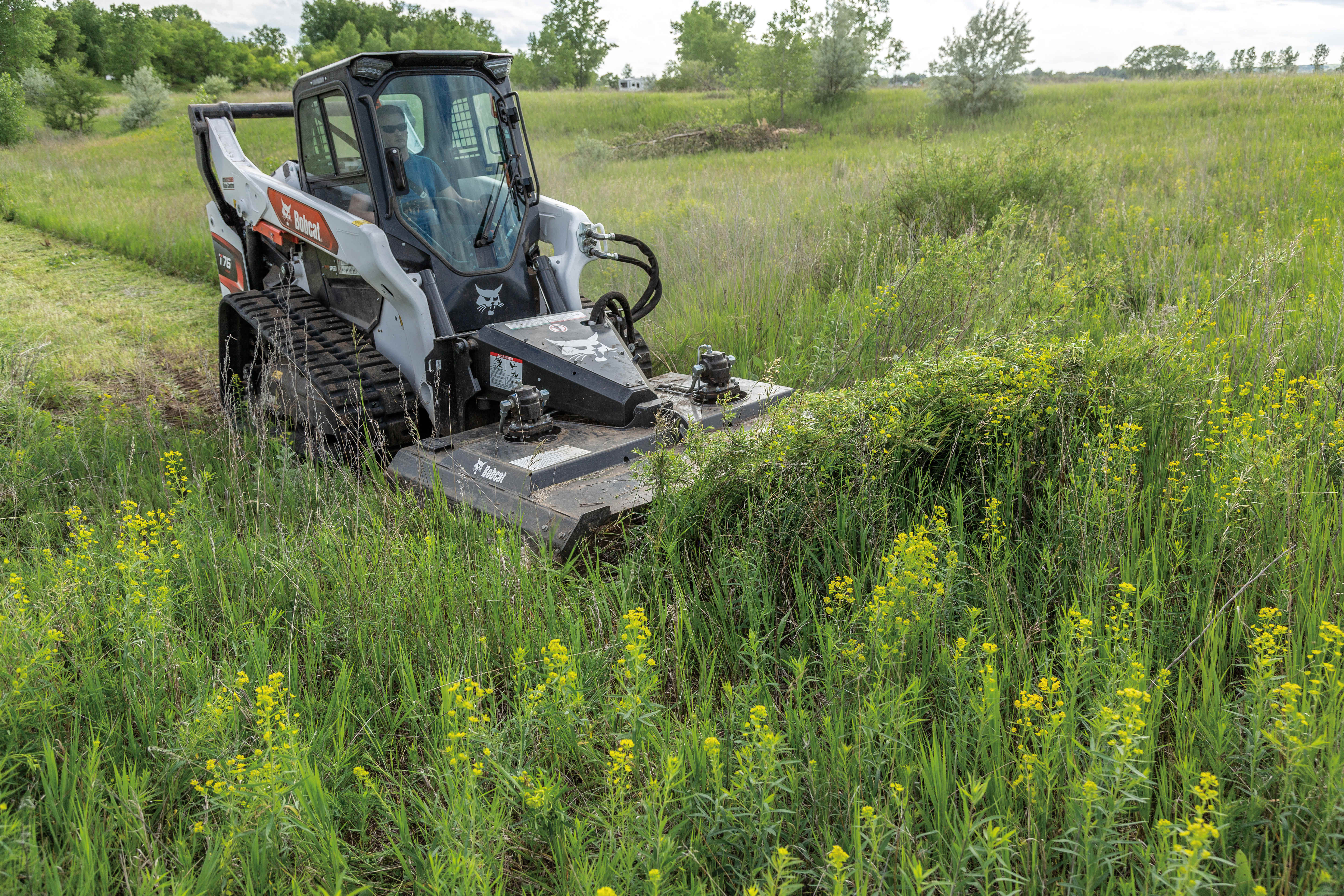 Operator Cuts Down Overgrown Weeds With a Bobcat T76 Compact Track Loader Equipped With a Brushcat Rotary Cutter Attachment