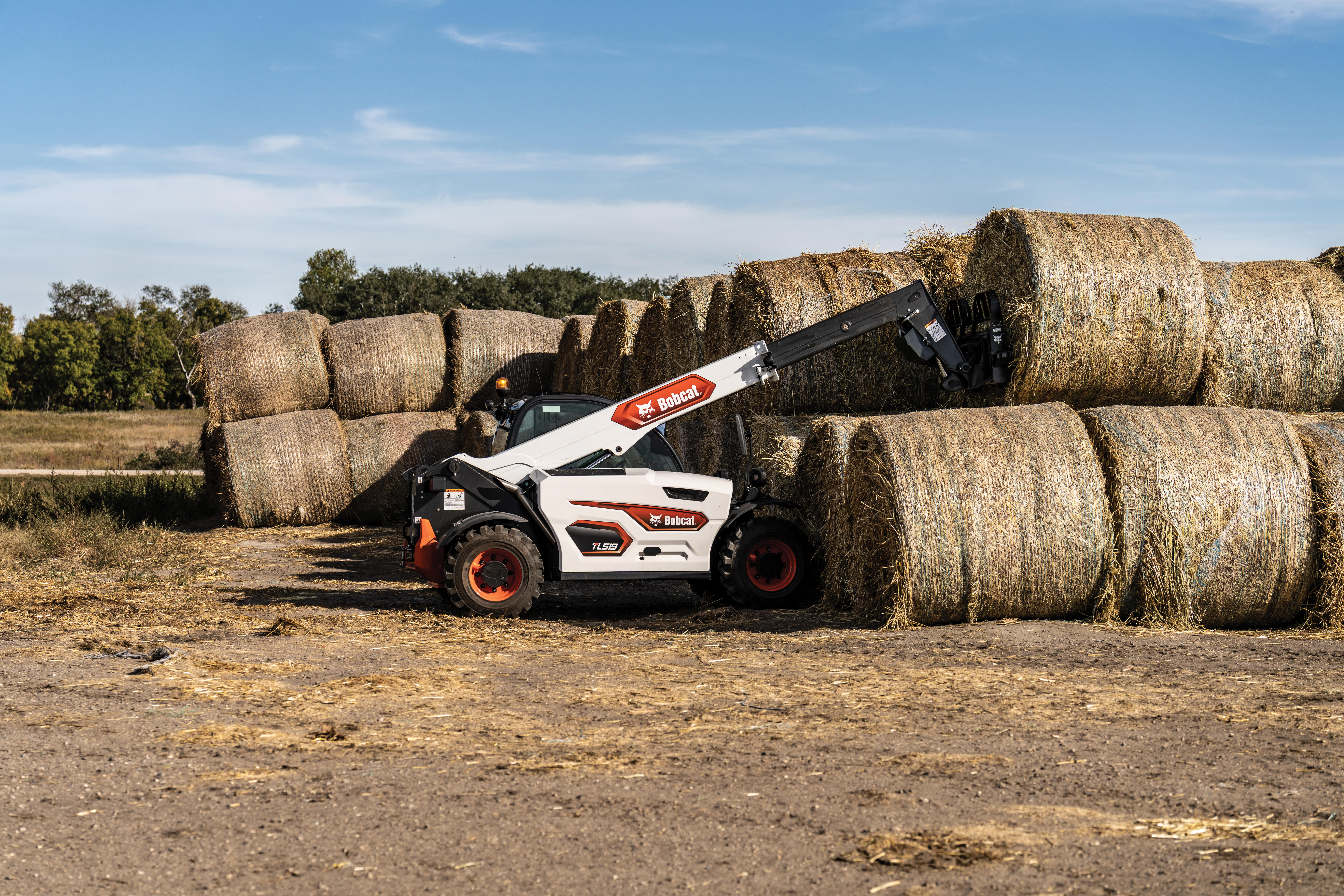 An Operator Stacks Round Hay Bales Using a Bobcat TL519 Telehandler With a Bale Fork Attachment in a Rural Field