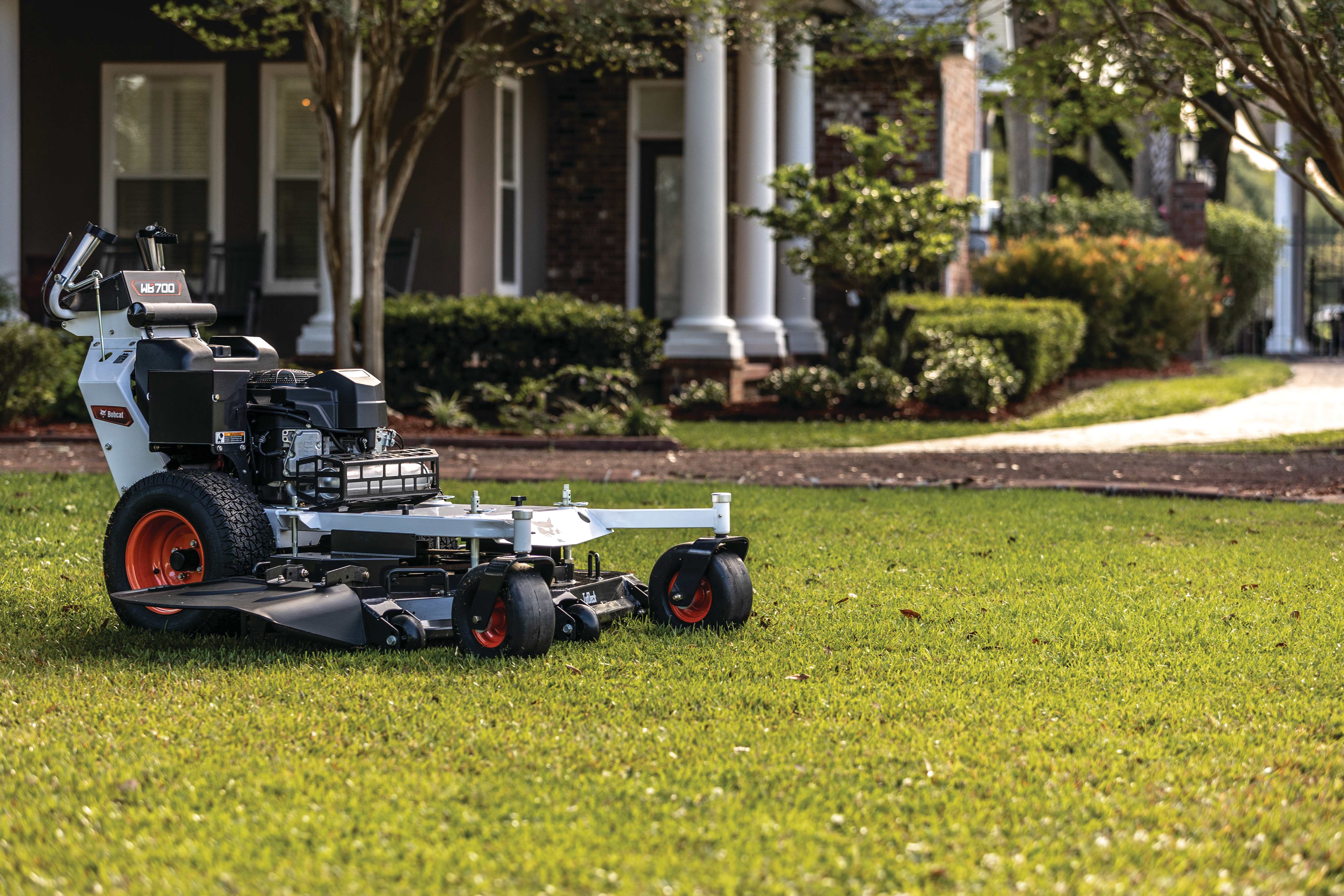 Hero image of Bobcat WB700 walk-behind mower sitting on freshly mowed lawn in front of beautiful home