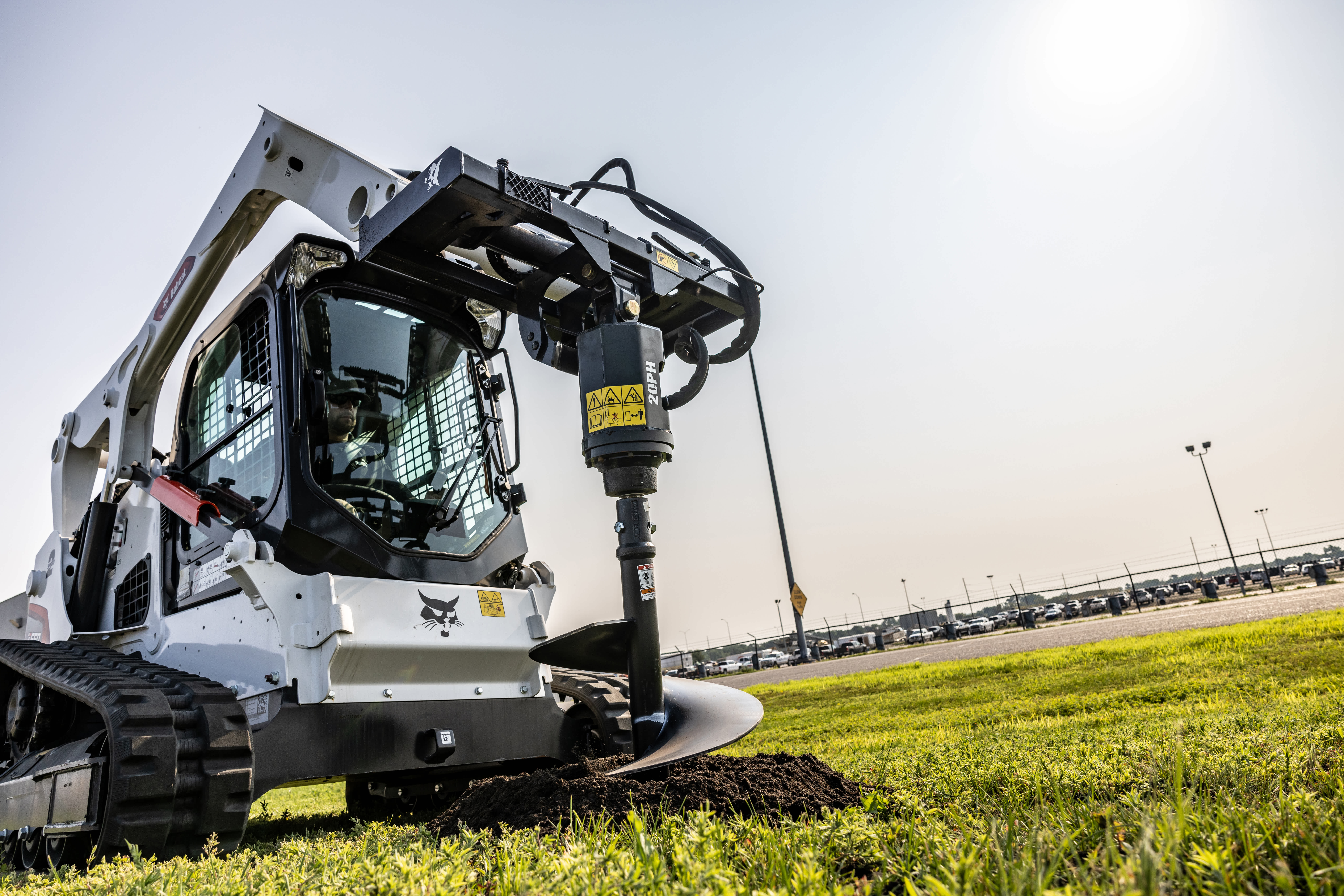 An Operator Digs Into a Grassy Lot Using a Bobcat Compact Track Loader With an Auger Attachment