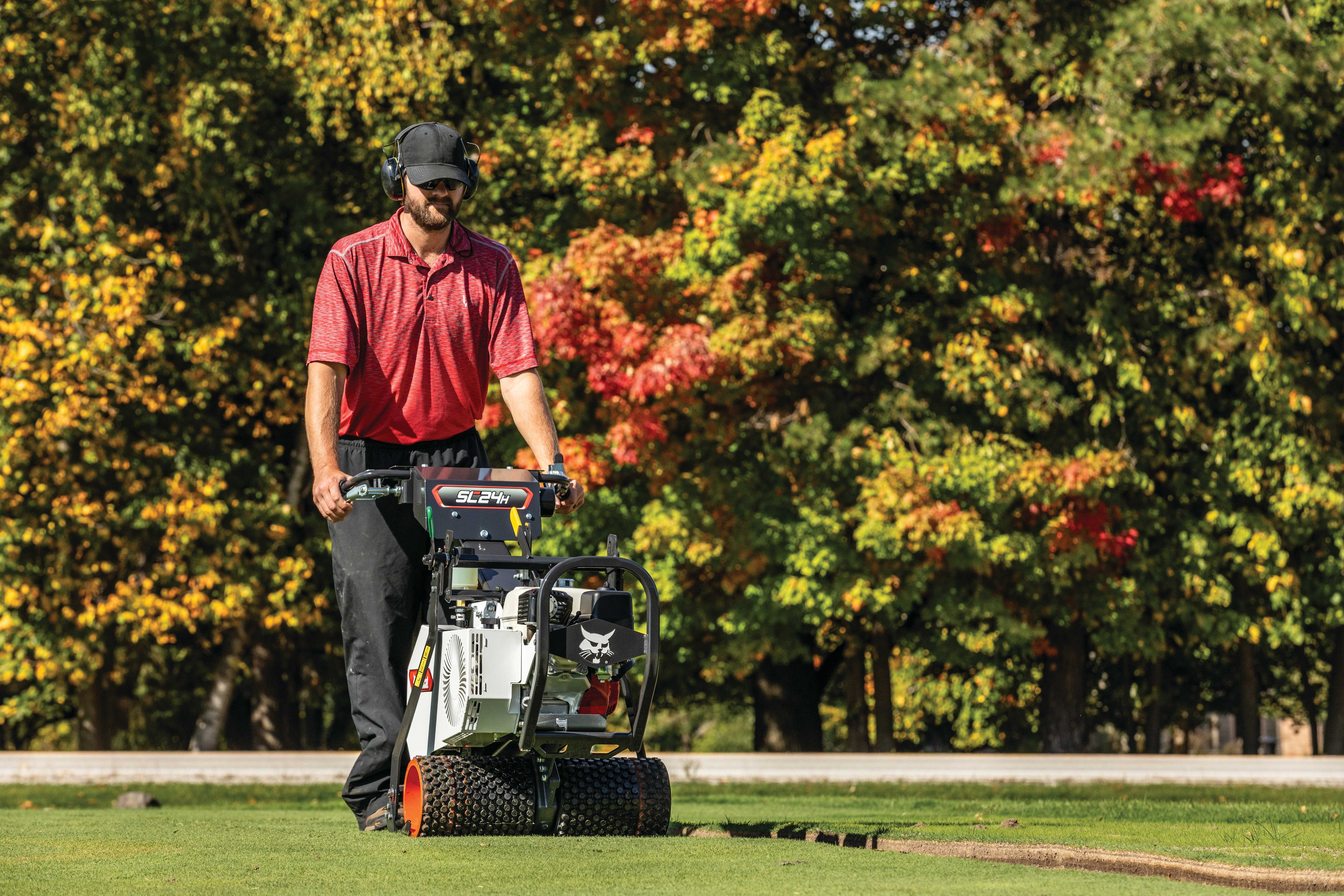 Man cutting strips of sod with the Bobcat SC24H sod cutter with a road and trees displaying autumn colors in the background