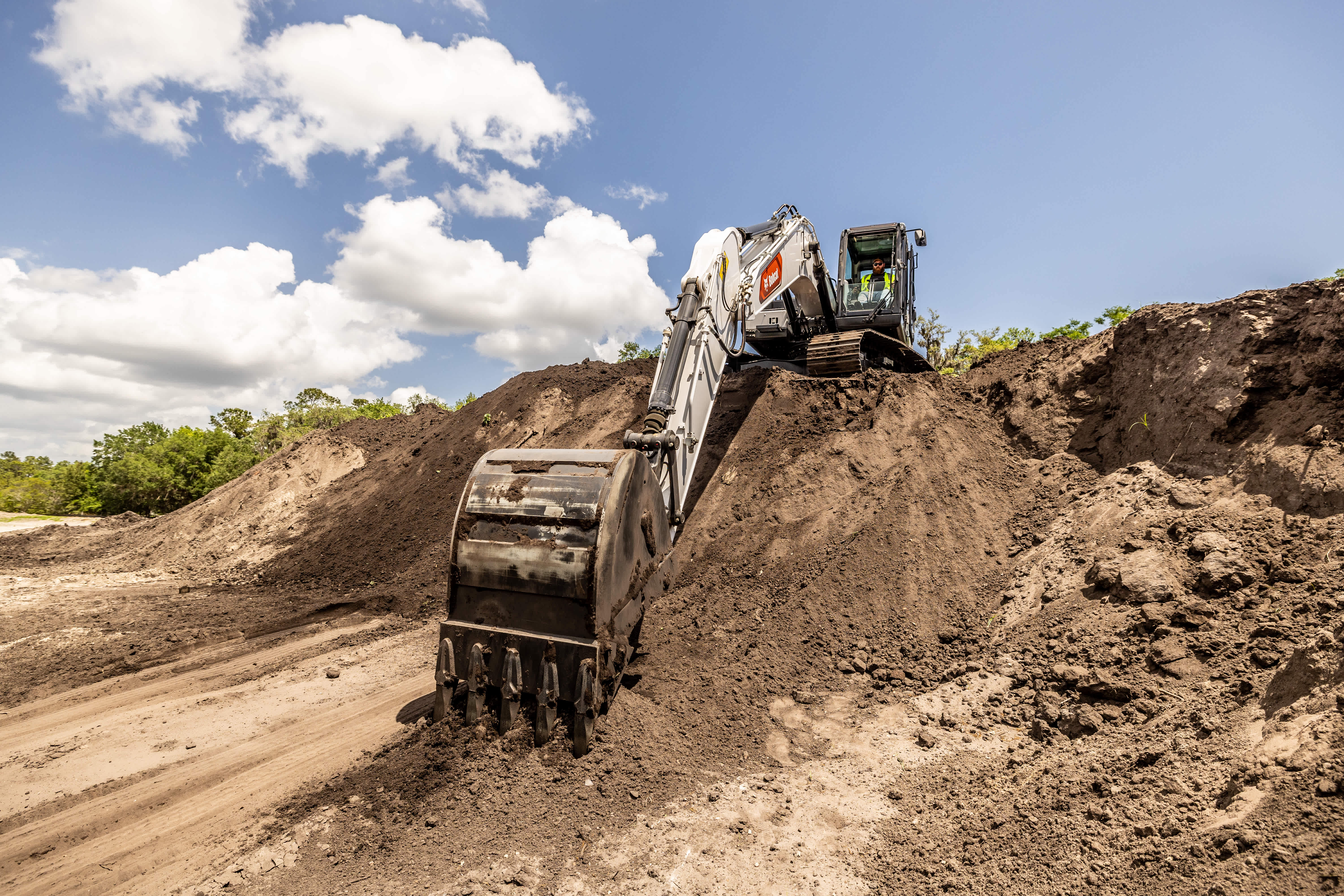 Bobcat E220 Large Excavator With Bucket Attachment Excavating a Large Soil Pile With an Operator in the Cab