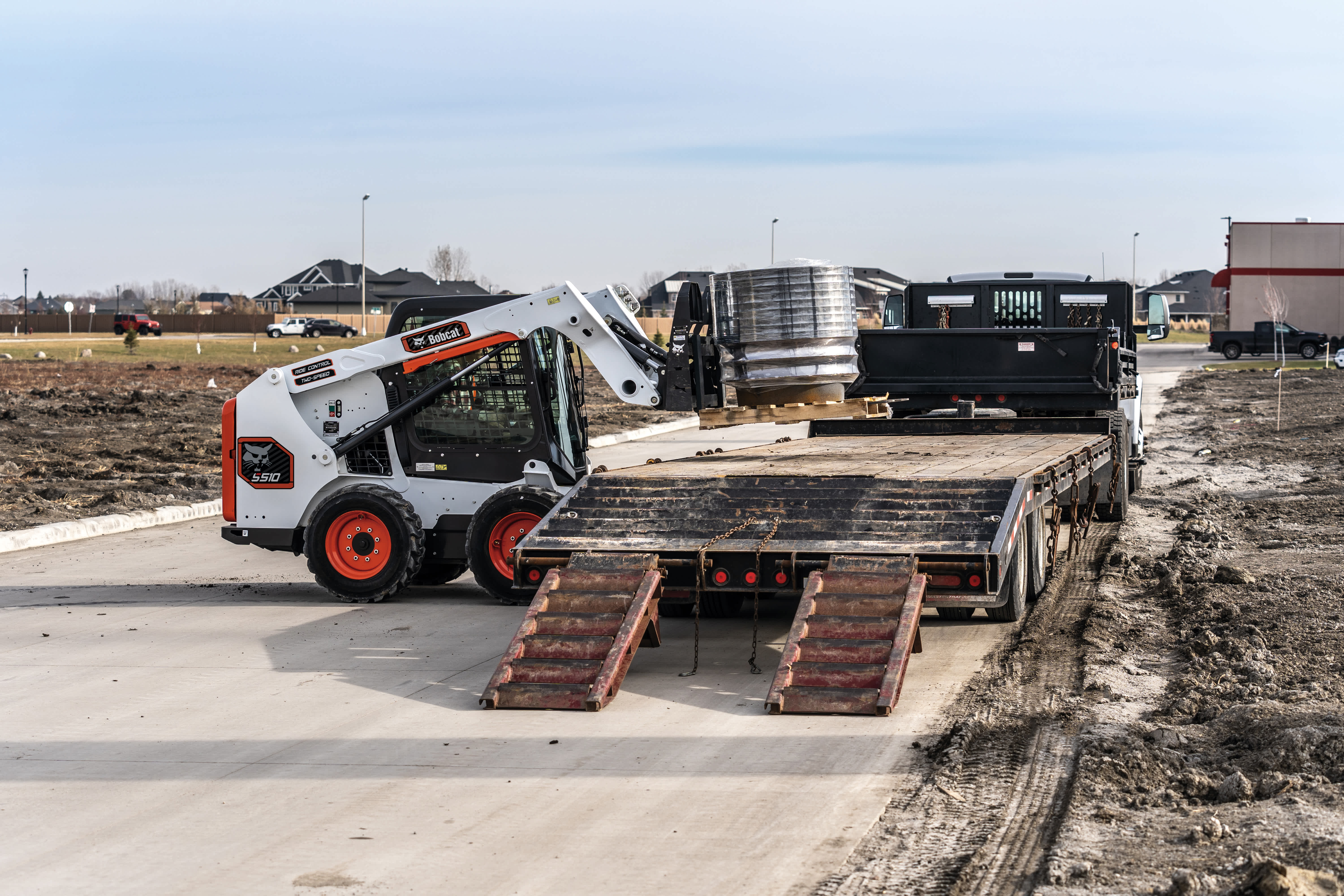 An Operator Transports a Pallet Load Using a Bobcat S510 with a Pallet Fork Attachment at a Jobsite