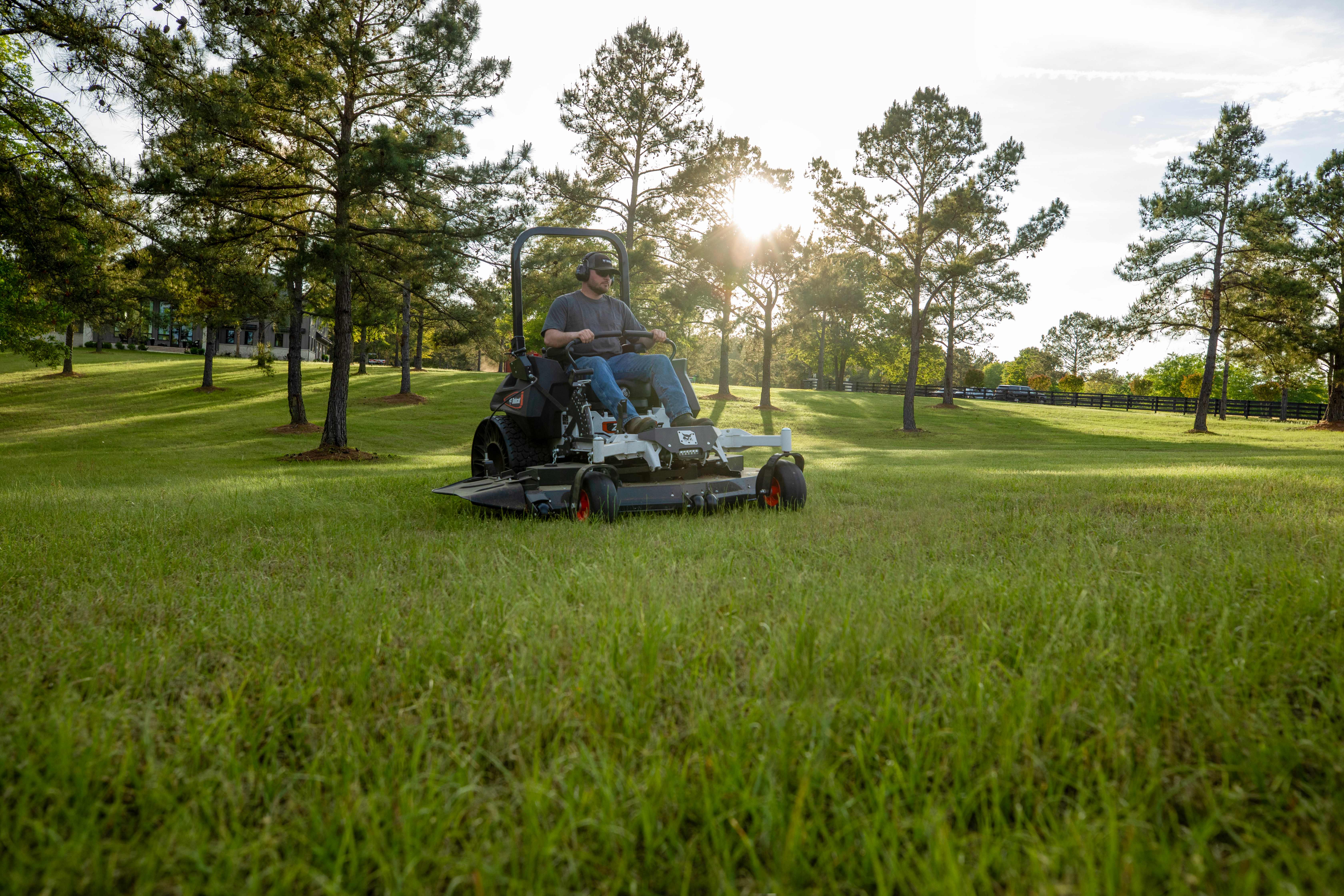 Bobcat ZT7000 zero-turn riding mower in action with male operator mowing large homeowner property in the early morning as the sun is rising